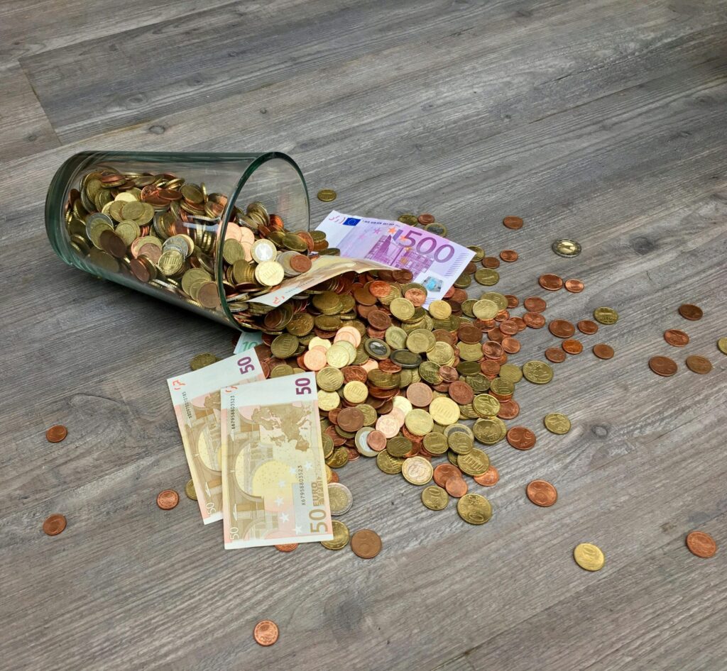 Coins and paper bills spill on the table when the glass container tilted. 