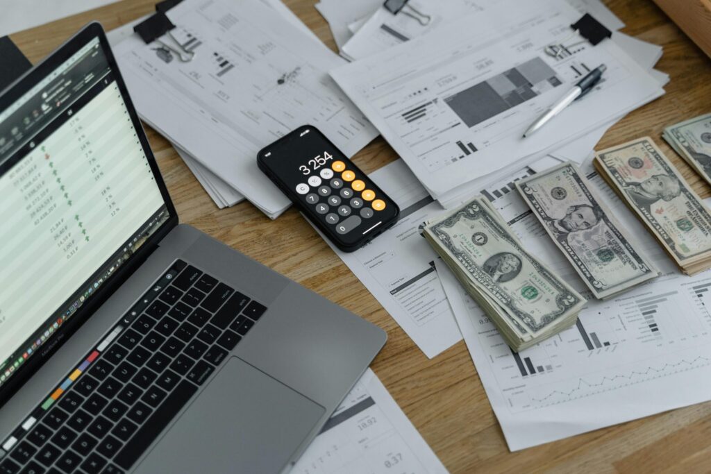 A laptop, calculator, and money spread on the table. Photo by Tima Miroshnichenko